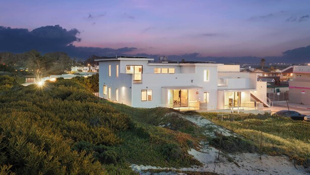 Een modern huis met twee verdiepingen, een plat dak, grote ramen en een zichtbare trap die naar de bovenverdieping leidt.