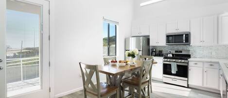 A modern kitchen with white cabinets, a stainless steel refrigerator, a microwave, and a stove. There is a dining table with chairs and a vase of flowers.