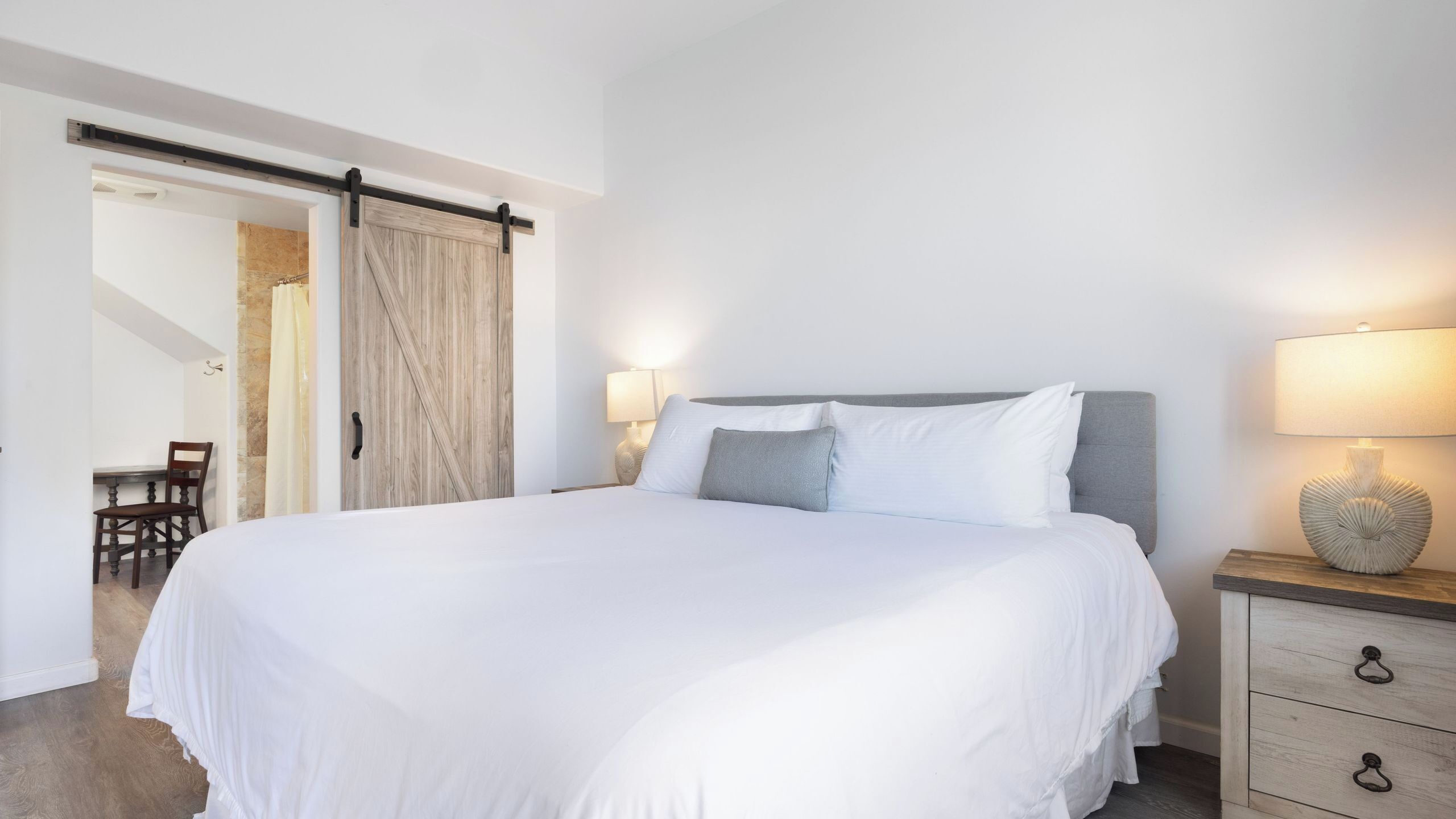 Un dormitorio con cama, mesita de noche, lámpara y una puerta corredera que da a otra habitación.