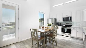 Een moderne keuken met witte kastjes, een roestvrijstalen koelkast, een magnetron en een oven. Er is een eettafel met stoelen en een raam met uitzicht op de omgeving.