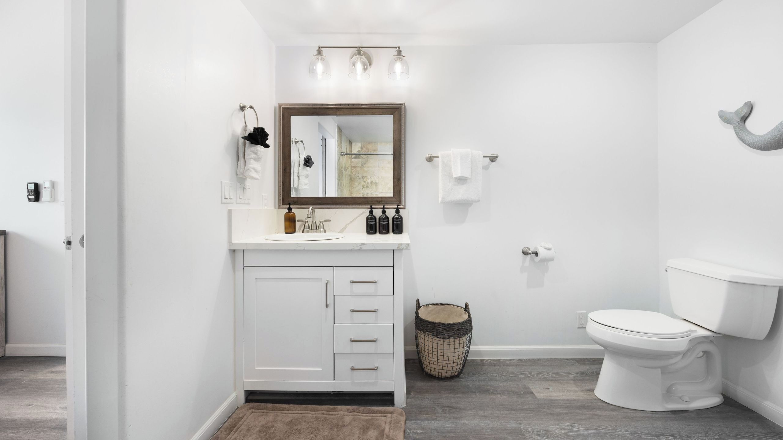 Un bagno moderno con un mobile lavabo bianco, uno specchio grande, un water e un piccolo cesto in vimini.