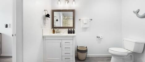 Un bagno moderno con un mobile lavabo bianco, uno specchio grande, un water e un piccolo cesto in vimini.