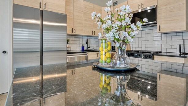 Una cocina moderna con armarios de madera clara, un refrigerador de acero inoxidable, una estufa y una encimera de mármol.