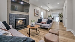 Una sala de estar moderna con chimenea, un conjunto de sofás, una mesa de centro y un televisor montado en la pared.