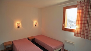 Een kleine, eenvoudige kamer met twee eenpersoonsbedden, een raam met uitzicht en twee wandlampen.