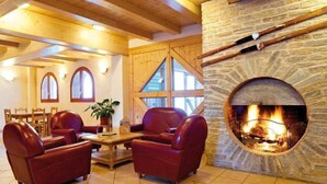 Een knus interieur met een stenen openhaard, leren banken, houten balken en een eethoek.