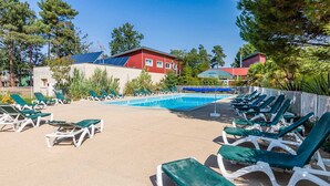 Un área de piscina con sillones de descanso, una piscina y un edificio rojo al fondo.