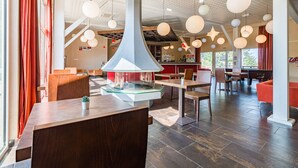 Un interior de restaurante moderno con mesas de madera, una mesa central con cubierta de vidrio y luces esféricas colgantes.