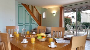 Een ontbijtruimte met een houten tafel, gedekt met fruit, gebak en sinaasappelsap.