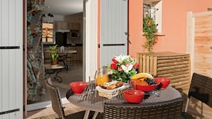 Un área de comedor al aire libre con sillas de mimbre, una mesa redonda y un desayuno que incluye frutas, pan y una jarra de jugo de naranja.