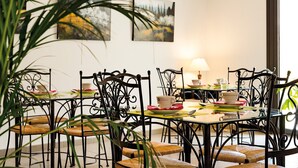 Un comedor con una mesa redonda, sillas de metal negro y un tablero de vidrio. Hay dos cuadros en la pared, una lámpara sobre la mesa y una planta al frente.