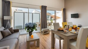 Un salon moderne avec un canapé, une table basse sur laquelle est posée une bougie, et un coin repas avec des éléments pour le petit-déjeuner.
