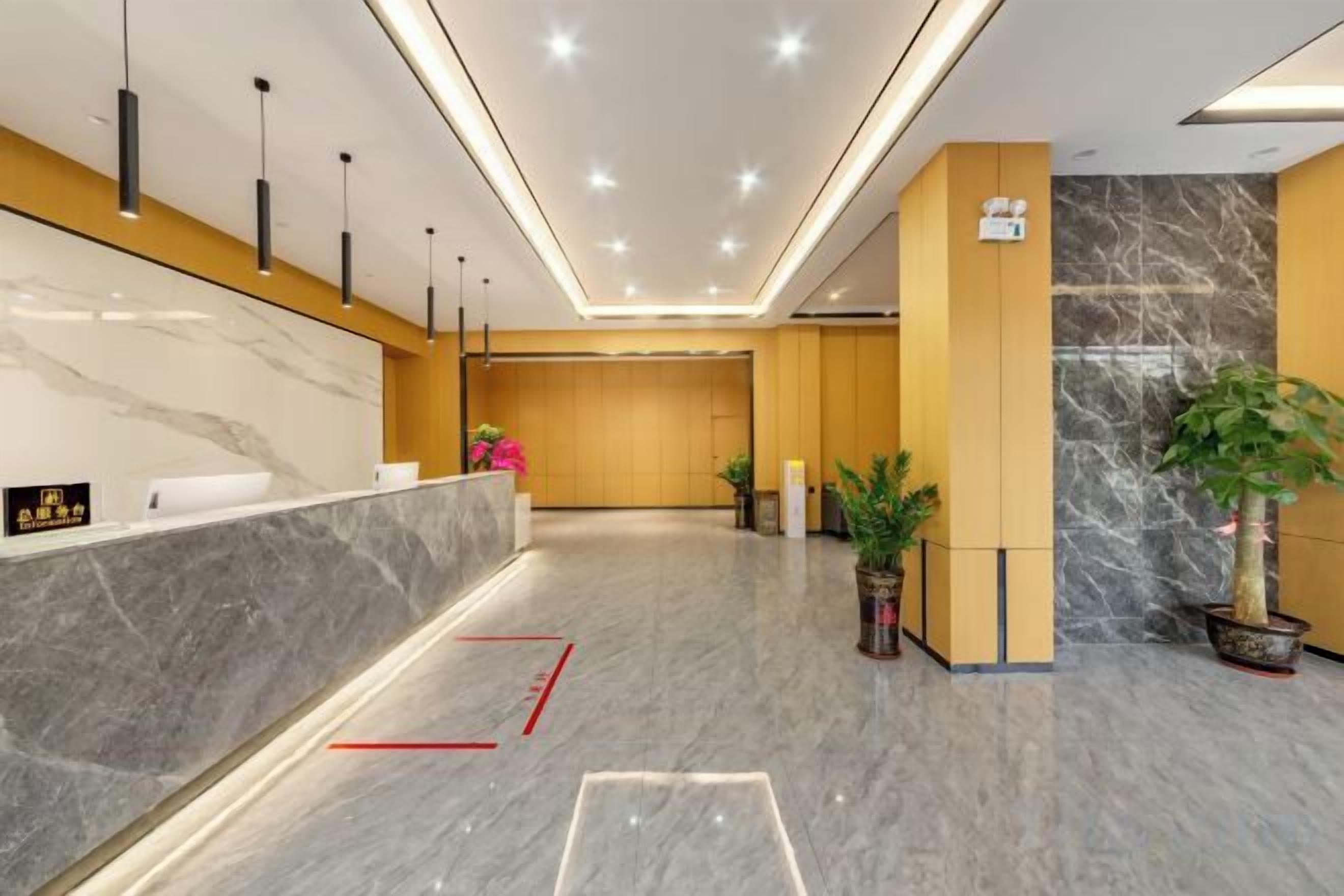 A hotel reception area with a marble counter, modern pendant lighting, and potted plants.