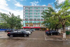 Ein mehrgeschossiges Hotel mit Parkplatz vor der Tür, Bäume säumen die Straße, und der Himmel ist wolkenlos.