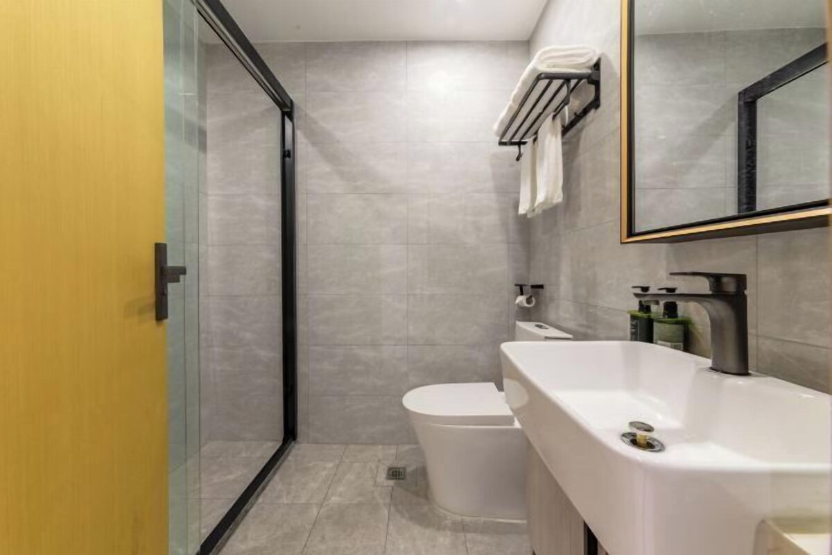 Un baño moderno con cabina de ducha de vidrio, inodoro blanco y un lavamanos grande con espejo superior.