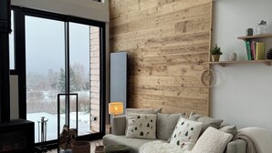 A modern living room with a large window, a fireplace, a wooden accent wall, and a cozy sofa. - Atypical chalet in the heart of the Auvergne volcanoes (Saint-Genès-Champespe)
