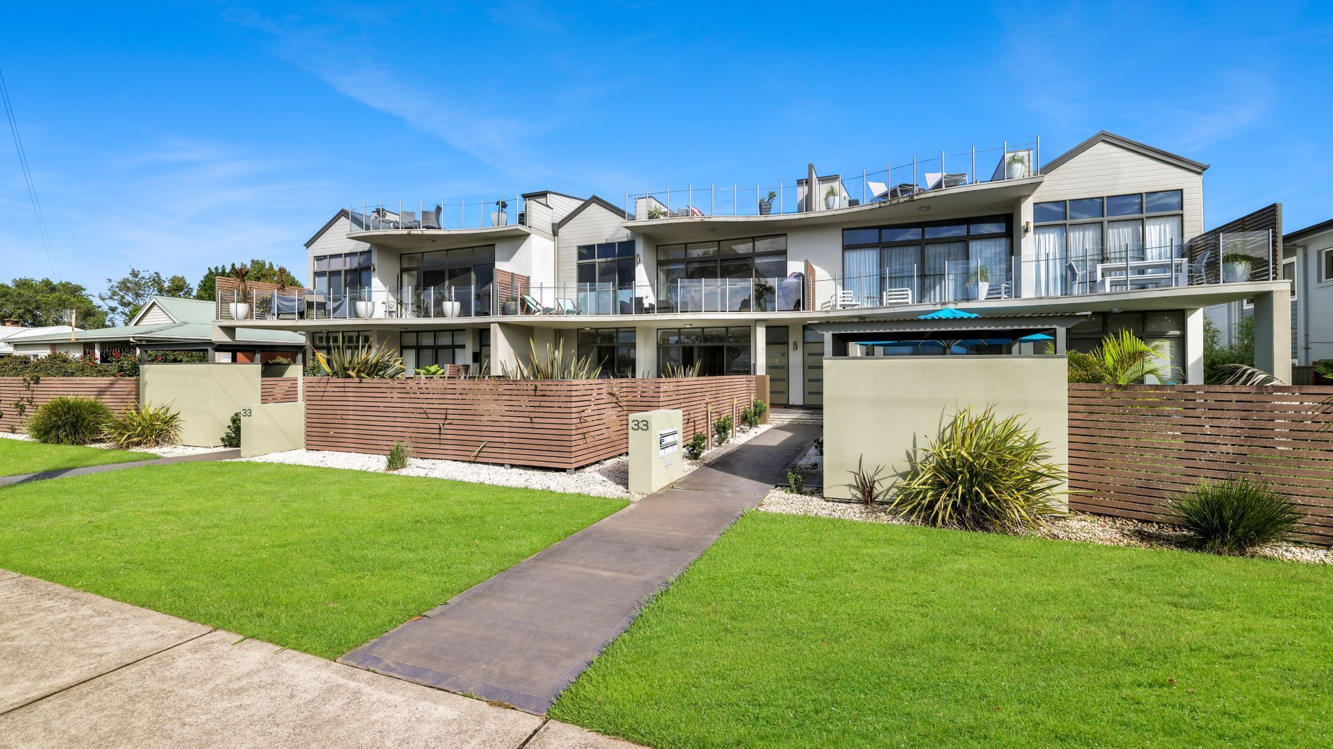 A modern two-story house with a flat roof, large windows, and a balcony.