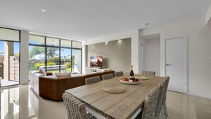 A modern living room with a large dining table, comfortable seating, and a television. - Our Beach House at Husky by Book Jervis Bay - Coastal Couples Escape (Huskisson)