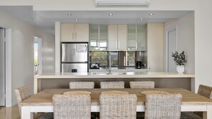 A modern kitchen with stainless steel appliances, a central island with seating, and a view of the outdoors. - Our Beach House at Husky by Book Jervis Bay - Coastal Couples Escape (Huskisson)