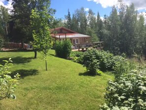 A house with a red roof, surrounded by a well-maintained lawn and various shrubs. - Moose Mountain Cabin - Cozy Retreat with Aurora Views  (Fairbanks)