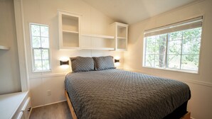 A bedroom with a bed, built-in shelving above, and two windows.