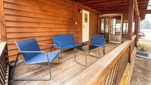 A wooden porch with a railing, a door, and three blue chairs with metal frames.