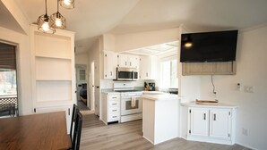 A modern kitchen with white cabinetry, a central island, a microwave, and a flat-screen TV mounted on the wall.