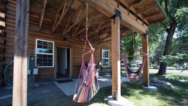 A wooden cabin with a porch, two hammocks, and a small patio area.
