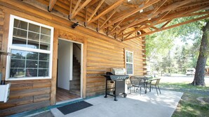 A wooden cabin with a covered patio, a grill, and a table with chairs.