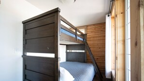 A bunk bed with a wooden frame and a grey bedspread in a room with wooden walls and a window.
