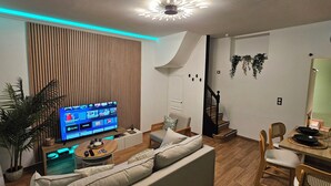 A modern living room with a flat-screen TV, a sofa, a dining table set for four, and a staircase. - L'Hortillon (Amiens)