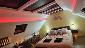 A bedroom with a sloped ceiling, a bed with rose petals, a nightstand with a lamp, and a wall-mounted decoration. - L'Hortillon (Amiens)