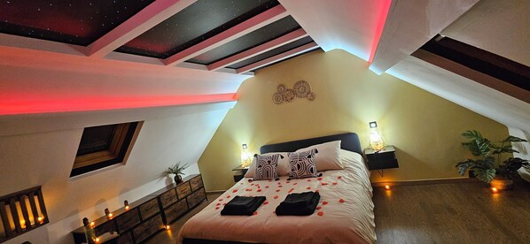 Camera da letto con soffitto spiovente, un letto con petali di rosa, un comodino con una lampada e una decorazione a parete.