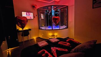 Ett svagt upplyst rum med en massagebänk, hjärtformade ballonger och en tv-skärm som visar en spellista med romantisk musik.