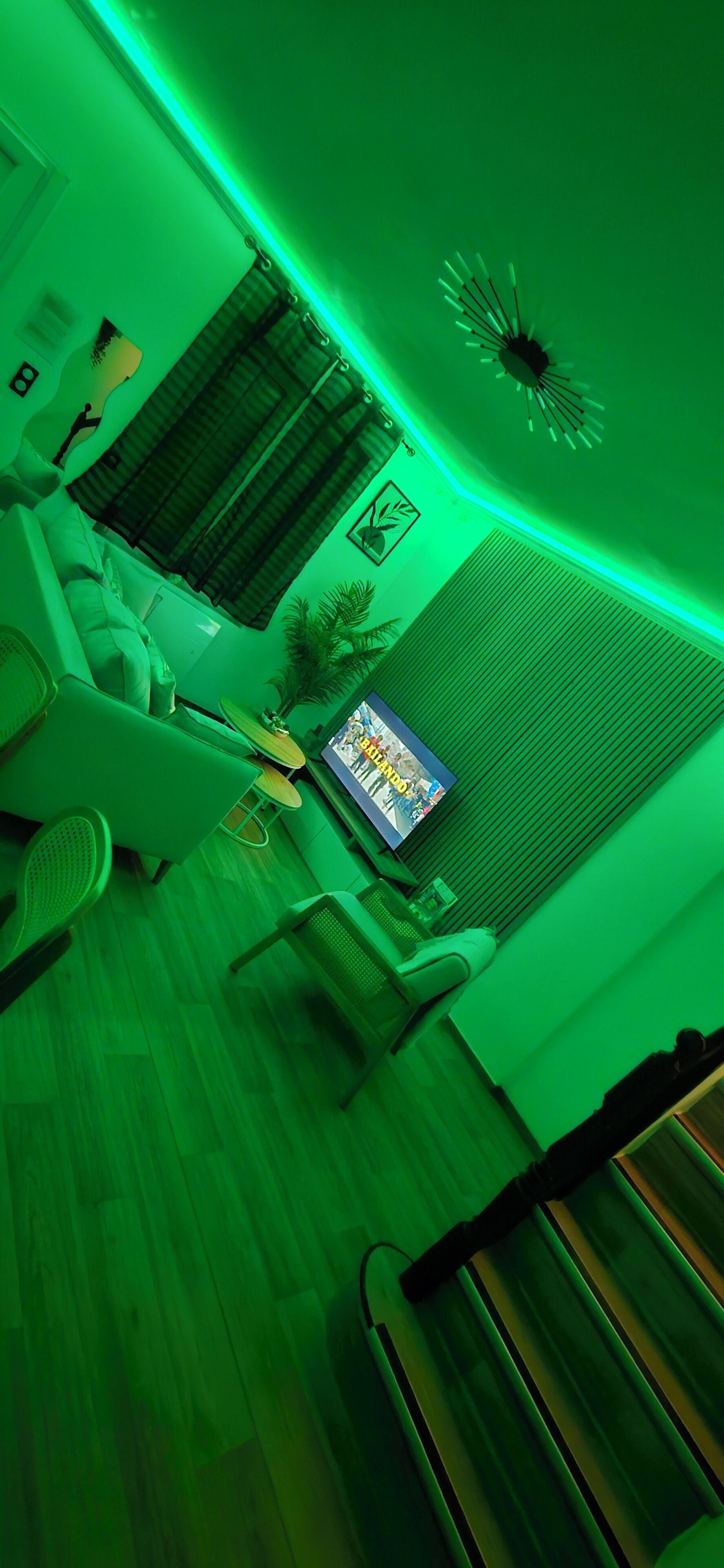 Ein Wohnzimmer mit sanfter grüner Beleuchtung, einem Fernseher, einem Sofa und einem Wandbild.
