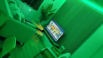 Ein Wohnzimmer mit sanfter grüner Beleuchtung, einem Fernseher, einem Sofa und einem Wandbild.