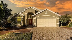 A two-story house with a garage, a front entrance with a red door, and a driveway leading to the garage. - Luxe Lakeside Escape (Davenport)