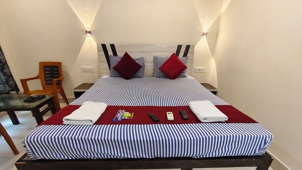 Une chambre d’hôtel avec un lit, deux oreillers, une couverture rouge, une serviette blanche et une télécommande posée sur le lit.