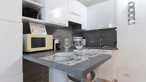 A modern kitchen with white cabinets, a microwave, a coffee maker, and a dining area with a marble countertop.