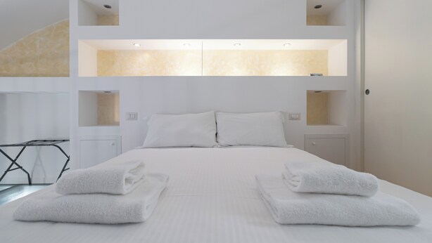 A modern hotel room with a large bed, two bedside tables, and built-in shelves above the bed.