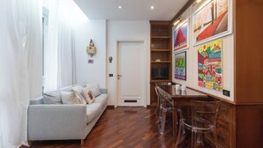 A living room with a grey sofa, a wooden coffee table, and a TV. There are colorful paintings on the wall and a white door. - Italianway Easy - Garibaldi 49 (Milano)