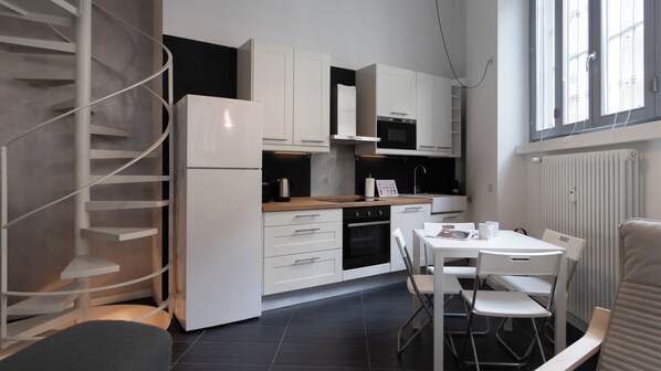 A modern kitchen with white cabinetry, a built-in oven, and a dining area with a table and chairs. - Italianway Easy - Carcano 27 (Milano)