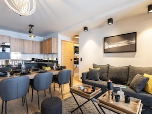 Un salon moderne avec un canapé gris, une table basse et un coin repas comprenant des chaises et une table mise pour le repas.