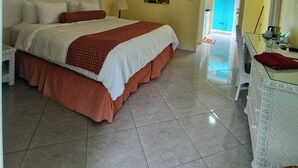 A hotel room with a bed, a desk, a chair, a ceiling fan, and a painting on the wall. - Charming 1-bedroom apartment with WiFi, AC, swimming pool, in lovely Soufrière (St lucia)