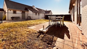 Ein Hinterhof mit einer Terrassentisch und -stühlen, einem eingezäunten Garten und einem Haus mit einem Ziegeldach.