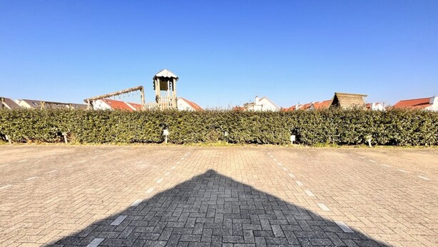 Ein gepflasterter Platz mit blauem Himmel, einem entfernten Turm und einer Hecke.