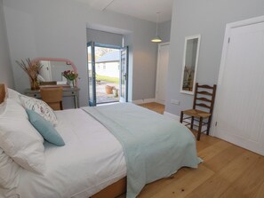 A bedroom with a bed, a desk, a chair, a mirror, and a door leading to an outdoor area. - Stapleford Farm (Beaminster)