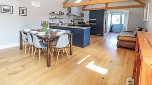 A spacious kitchen with wooden beams, a dining area with a table and chairs, and a view of the outdoors. - Stapleford Farm (Beaminster)