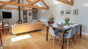 A spacious loft with high ceilings, exposed wooden beams, a cozy seating area, a dining table set for six, and a fireplace. - Stapleford Farm (Beaminster)