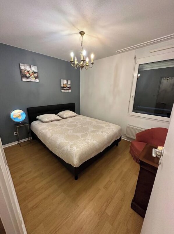 A bedroom with a bed, a globe on a side table, a red chair, and a window.